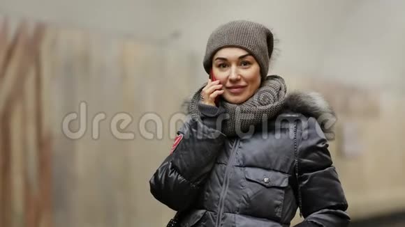 穿着冬装带着手机的女孩在地铁站的站台上微笑视频的预览图
