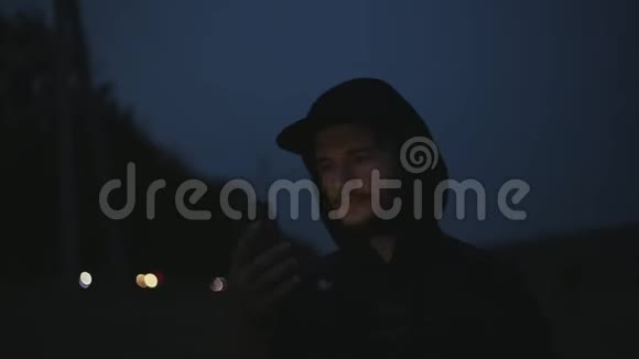 一个年轻严肃的男人晚上站在街上手里拿着智能手机视频的预览图