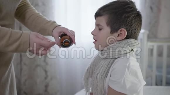 父母照顾健康的孩子母亲把咳嗽糖浆倒入勺子里为生病的小男孩吃药视频的预览图