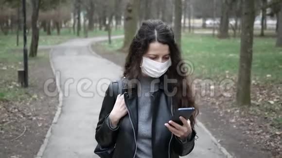 戴面具的年轻女子沿着公园和街道走使用电话防止病毒微生物的传播流行冠状病毒视频的预览图