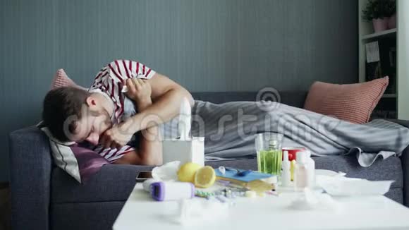 一个生病的年轻人试图在生病时睡着躺在公寓的沙发上躺在温暖的毯子下视频的预览图