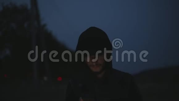一个年轻严肃的男人晚上站在街上手里拿着智能手机视频的预览图