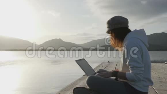 网络自由职业选择概念一位年轻女性在日落时分坐在湖边的码头上的笔记本电脑上工作视频的预览图
