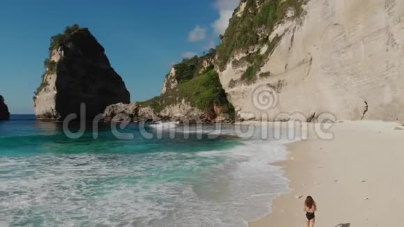 穿着黑色比基尼的女人在海滩上散步海滩上有海石和绿松石的海洋蓝天努沙佩尼达岛Atuh海滩视频的预览图