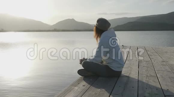 站在一个古老的木墩上一位从侧面看到长发的年轻女子在日落时看着湖面视频的预览图