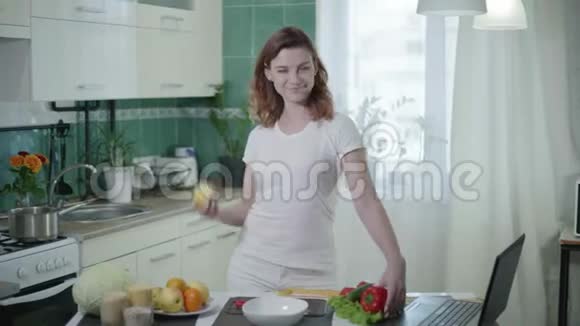 成功节食后的微笑女孩在厨房拿着健康食品摆姿势用胶带量着腰视频的预览图