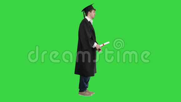 身着毕业礼服的男子在绿色屏幕上为摄像机摆姿势chroma键视频的预览图