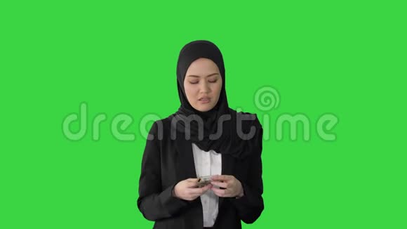 戴着头巾的漂亮女人走路在绿色屏幕上数钱Chroma键视频的预览图
