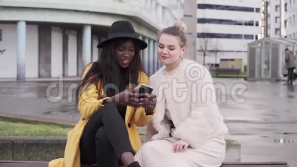 两个北欧女孩和一个黑人非裔美国女孩使用手机坐在城市的长凳上视频的预览图