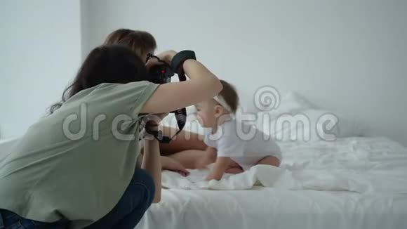 年轻的妈妈在摄影的时候在床上玩着拥抱婴儿视频的预览图