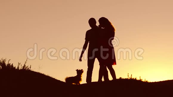 恋爱中的情侣在自然日落和接吻时跳舞剪影爱的男人和女人与狗跳舞剪影缓慢视频的预览图
