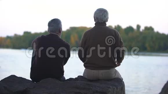 老年男性朋友坐在外面望着河的地平线宁静视频的预览图