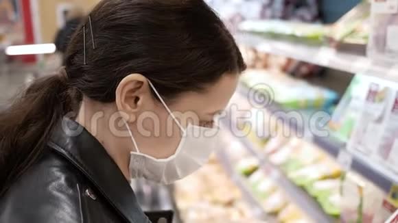 在杂货店里戴着医用口罩的漂亮黑发年轻女人大流行病选择产品视频的预览图