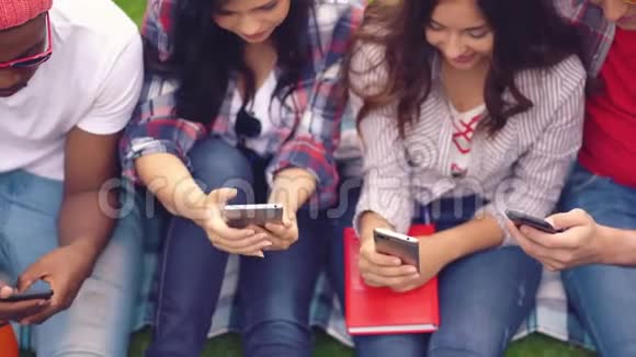 不同种族的年轻学生坐着挑选智能手机视频的预览图