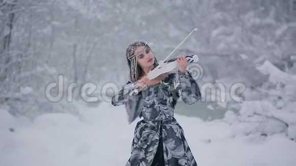 身穿灰色皇室礼服的童话形象可爱年轻女子在雪地上拉着白色小提琴视频的预览图