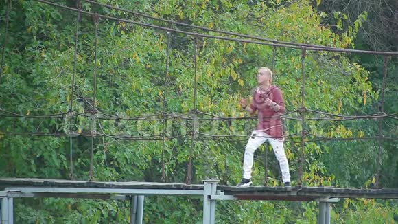 在美丽的画报上一位英俊的金发男子站在河上的吊桥上唱歌视频的预览图