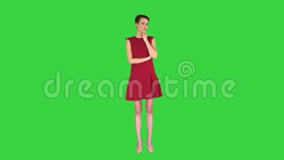 漂亮的年轻女人穿着红色的裙子站着听着有人在绿色屏幕上说话Chroma键视频的预览图