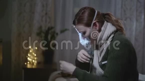 戴暖和围巾的生病女孩在家里坐在床上测量体温和吸入面罩视频的预览图