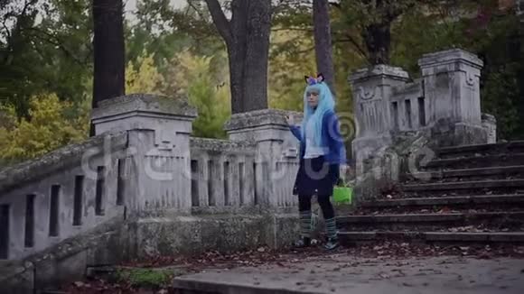 快乐的小女孩蓝色的头发穿着独角兽的万圣节服装带着糖果桶走下楼梯视频的预览图