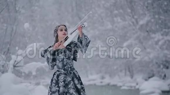 身穿灰色皇室礼服的童话形象可爱年轻女子在雪地上拉着白色小提琴视频的预览图
