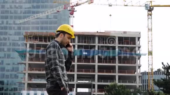 戴着防护头盔的工程师在一个建筑工地上走着在电话里交谈视频的预览图