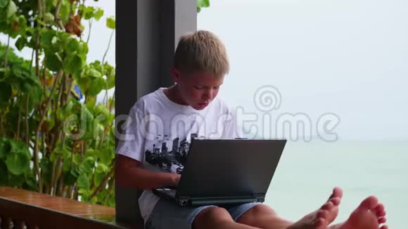 年轻人在笔记本电脑上玩坐在露台上靠近大海和海滩视频的预览图