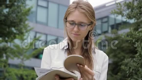 微笑的女人坐在办公楼旁的长凳上看杂志视频的预览图