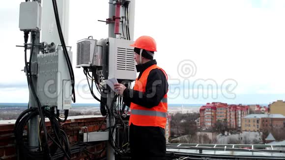 技术工人男性穿着明亮的防护服在天线附近的屋顶上工作并在笔记本上做笔记视频的预览图