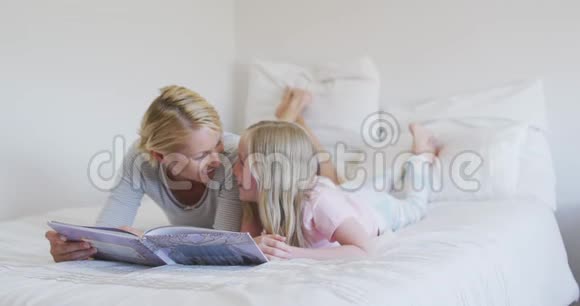 一个白人妇女在床上给女儿读故事的侧视图视频的预览图