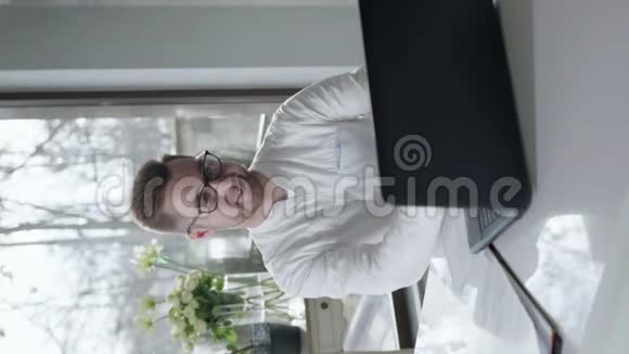 戴眼镜使用笔记本电脑上网的年轻商人坐在白办公室的桌子旁视频的预览图