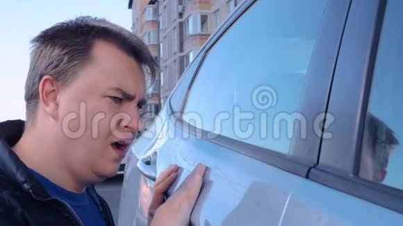 一个悲伤的家伙检查他的车门油漆上的划痕人类在叹息和咒骂期待着与保险的纠纷视频的预览图