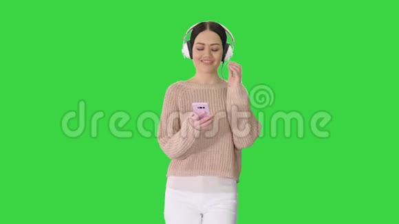 快乐女孩走路听音乐与智能手机戴耳机在绿色屏幕Chroma键视频的预览图