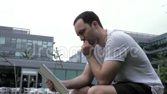 坐在户外使用数码平板电脑的严肃休闲男士视频的预览图