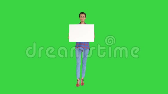 微笑美丽的女孩看着相机拿着一个空白的白色横幅在绿色的屏幕色度键视频的预览图