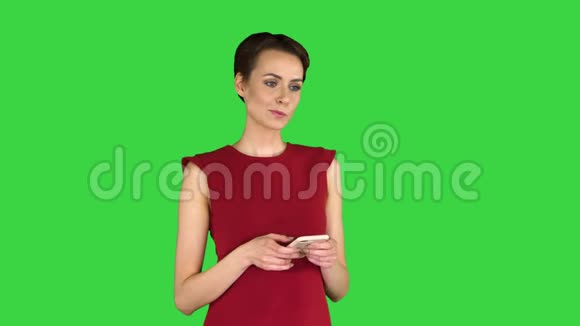 年轻快乐迷人的女性穿着红色连衣裙在绿色屏幕上发短信Chroma键视频的预览图