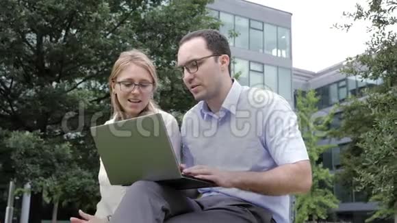 戴眼镜穿便装带笔记本电脑的英俊青年和他聪明迷人的同事在讨论视频的预览图