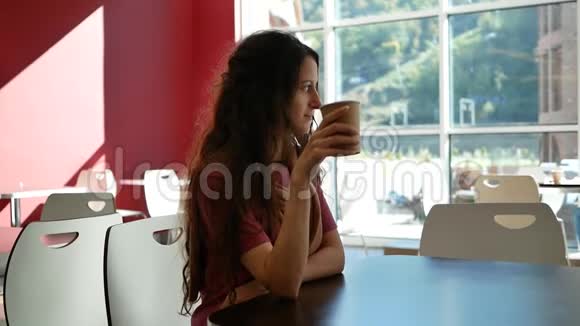 在咖啡馆度假的美丽年轻女子从纸杯里喝咖啡望着窗外视频的预览图