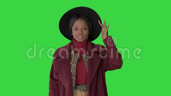 可爱的非洲模特穿着外套触摸帽子走在绿色屏幕上Chroma键视频的预览图