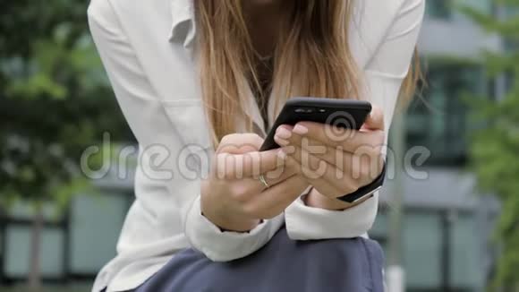 女人坐在公园的长凳上在手机里输入一条信息特写双手视频的预览图