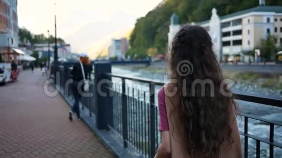 美丽的年轻女子背靠背站着在群山中的度假小镇的背景上转镜头视频的预览图