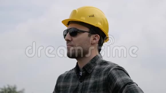 建筑工人白种人戴着头盔和太阳镜背景是一个阳光明媚的夏季工地视频的预览图