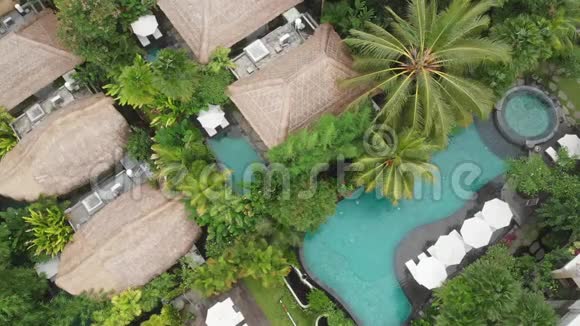 带草屋顶别墅和热带丛林和棕榈树的游泳池的豪华酒店的无人机鸟瞰豪华别墅视频的预览图