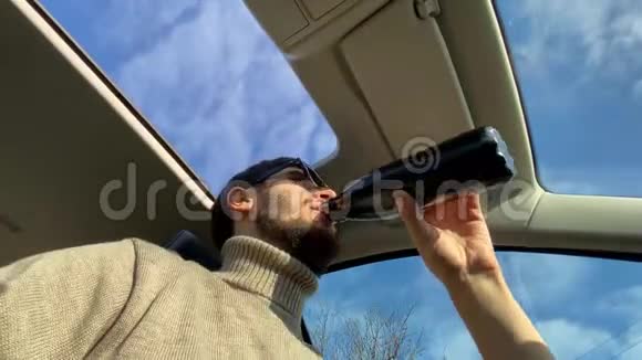 低角度视角的年轻开朗男子太阳镜饮用水从钢热生态瓶内车天空景色视频的预览图