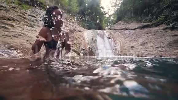 一位快乐的年轻女子坐在瀑布附近的一条小溪上视频的预览图