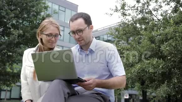 一起上网冲浪商务同事一起坐在长凳上看着笔记本电脑视频的预览图