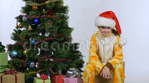 女孩一边做鬼脸一边坐在圣诞树旁用手捂着脸视频的预览图