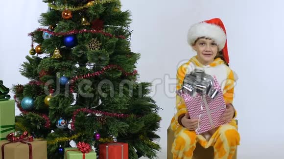 快乐的女孩坐在一个盒子上礼物放在新年树附近视频的预览图