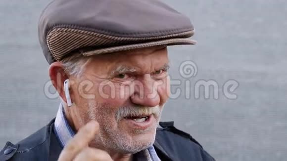 戴着帽子的霍利退休男子正双人敲击无线耳机打开音乐穿蓝色夹克的养老金领取者正在享受视频的预览图