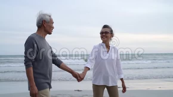 亚洲夫妇老年退休休息放松手牵手走日落海滩视频的预览图