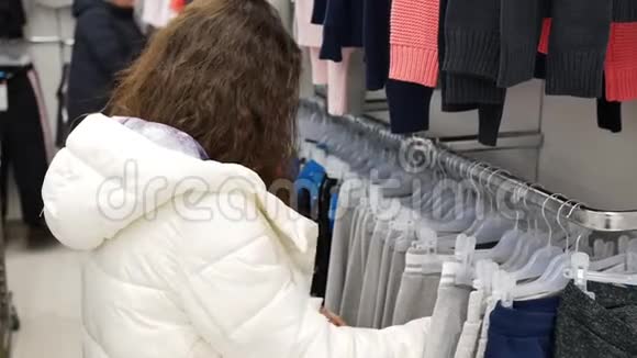 穿白夹克的年轻女子在商店里挑选衣服视频的预览图
